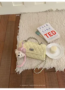 Elegant yellow quilted crossbody bag with cute teddy bear charm on a shaggy rug.