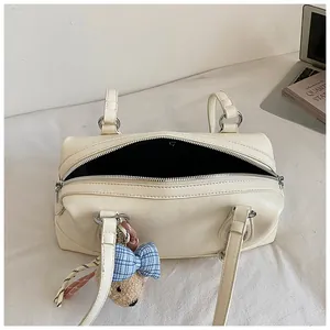 Close-up detail view of cream pillow handbag with cute teddy bear charm and open zipper.