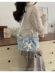 Detail of light blue denim crossbody bag with silver star charm worn by model