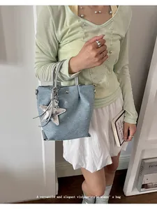 Detailed lifestyle shot of a light blue denim handbag featuring a silver star charm