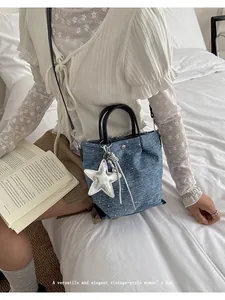 Close-up of a blue denim dumpling bag with a silver star charm held by a model on a bed