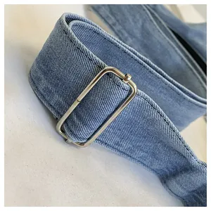 Detail view of a denim shoulder bag strap with an adjustable silver metal buckle.