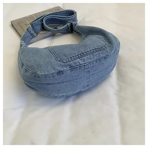 Detail showing the textured light blue denim crescent bag on white fabric background.