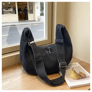 Close-up of a large black denim hobo bag with adjustable strap on a wooden table display