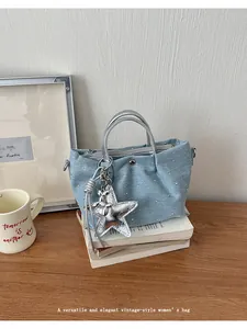 Detailed view of light blue denim dumpling handbag with silver star charm accessory