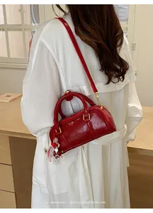 Detail of a red glossy cylinder handbag with chic cherry charm and gold-tone zippers.