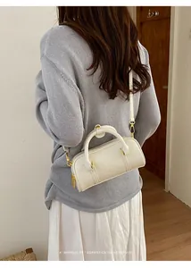 Close-up of a minimalist white leather pillow bag featuring top handles and golden hardware