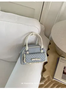 Détail d'un sac à main en denim bleu clair avec dentelle et nœud à pois sur un canapé blanc.