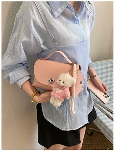 Detail view of a stylish pink textured leather crossbody bag with a cute teddy bear charm