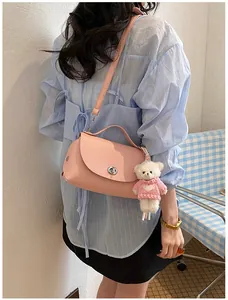 Detail of a pink textured leather crossbody bag worn by a model with a bear keychain