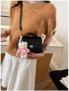 Detail of a black retro crossbody bag with a cute teddy bear charm worn by model.