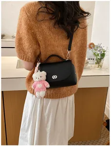 Back view of a vintage black textured leather crossbody bag with a cute bear keychain.