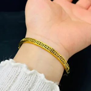 Macro view of a gold-plated stainless steel bangle with a hollow Greek key pattern