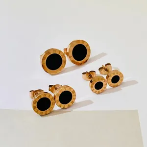 Macro view of three sizes of rose gold Roman numeral stud earrings with black centers