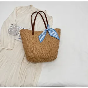 Détail d'un sac cabas en paille fait main avec foulard rayé bleu et anses marron.