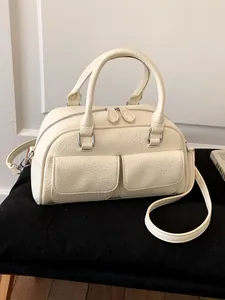 Elegant cream Boston handbag featuring two front pockets and an adjustable strap