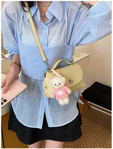 Detailed view of a beige vintage textured crossbody bag with a cute pink bear charm.