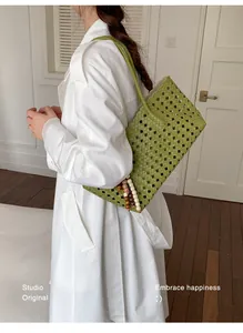 Large green woven cutout tote bag worn by a model in a stylish lifestyle setting.