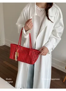 Stylish red woven hollow-out tote bag with beaded tassel carried by model in white coat