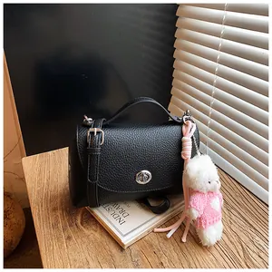 Close-up detail of a black pebbled leather crossbody bag with cute pink teddy bear charm