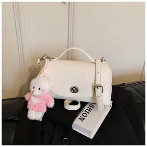 Detail of a white textured crossbody bag with a cute teddy bear plush keychain charm