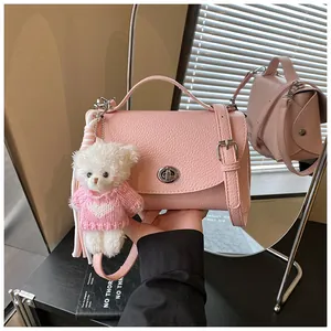 Detail of a pink pebbled crossbody bag with a cute plush bear charm in a stylish setting.