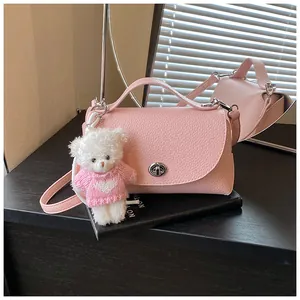Detail of a pink textured leather crossbody bag with a cute white teddy bear charm