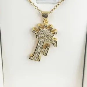 Close-up of gold-plated crown letter F pendant with clear zircon stones on a chain.