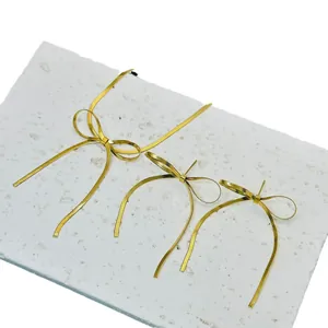Detail van gouden strikoorbellen met lange kwastjes op een witte stenen ondergrond.