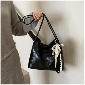 Detail of black glossy crinkle patent leather commuter tote bag with pearl lace charm