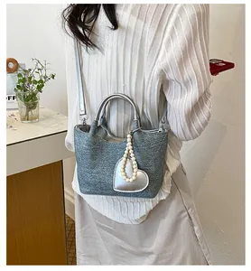 Detail view of a stylish textured bucket bag with heart pearl charm worn on the body.