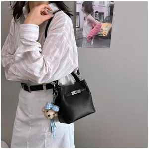 Vista detallada de un bolso tipo cubo de cuero negro de moda con dije de oso
