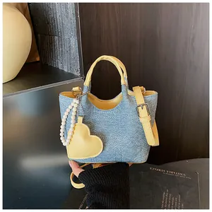 Close-up of a stylish blue denim handbag featuring yellow handles and a heart pearl charm.