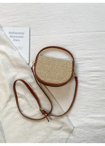 Top view of a woven straw saddle bag with brown leather trim on a white textured fabric