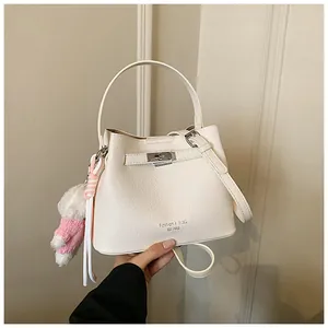 Elegant detail of a white pebble-textured bucket bag with cute plush teddy bear charm
