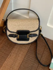 Stylish straw woven saddle bag with black leather trim and chic gold buckle details.