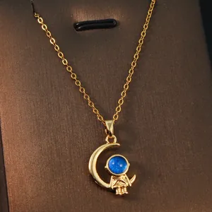 Detail view of a golden astronaut and crescent moon pendant with a blue gem center.