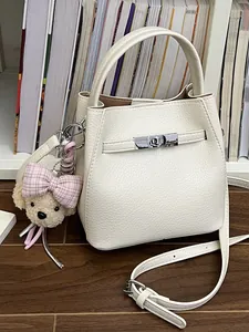 Elegante bolso tipo cubo de cuero blanco con dije de perro de peluche y correa bandolera