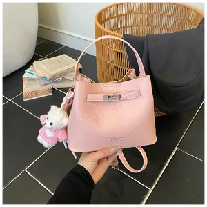 Detailed view of a pink litchi grain bucket bag featuring a silver lock and cute bear charm