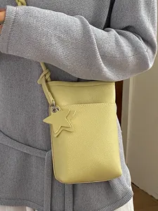 Modische gelbe Umhängetasche für das Handy mit Sternanhänger auf lila Pullover