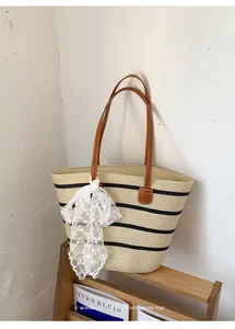 Detalle de un bolso tote de paja a rayas con correas de cuero marrón y encaje blanco