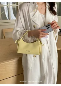 Close-up of a minimalist light yellow leather handbag held by a fashion model