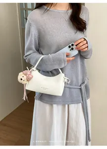Chic white crescent handbag with cute bow charm held by model in casual outfit