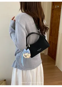 Close-up detail of a black chic shoulder bag styled with a cute puppy plush keychain.