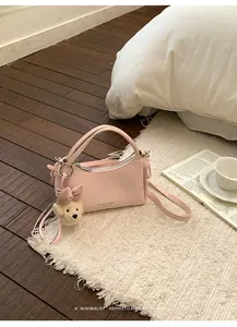 Elegant pink mini handbag with a cute teddy bear charm presented on a white cozy rug background