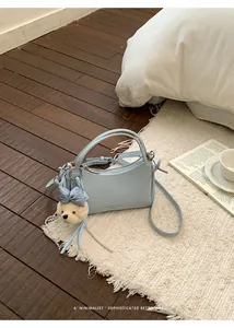 Detailed view of a light blue leather crossbody handbag with a cute bear charm on a rug