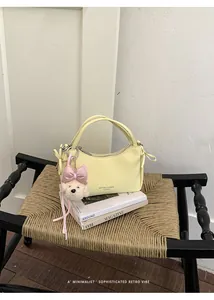 Stylish yellow mini handbag with cute bear charm on woven chair and magazines.