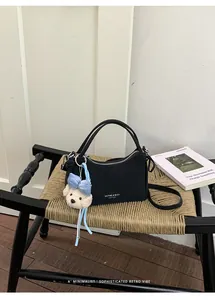Close-up detail of a black minimalist leather handbag featuring a cute plush bear charm