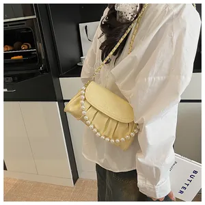 Primo piano di una borsa a mano gialla a pieghe con catena di perle su una modella.
