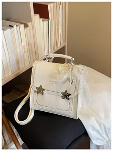 Dettaglio di uno zaino in pelle crema con fibbie a stella e fiocco di perle chic